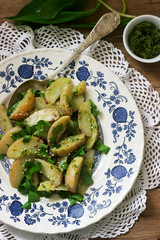 Vegetarian potato salad with wild garlic and pesto sauce on a wooden background. Rustic style.