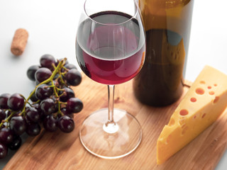 A glass with red wine, cheese, grapes and a bottle of wine on a light background. Light drink and snack