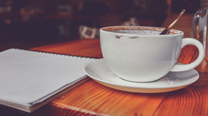 Cup of coffee with paper note pad on table in coffee cafe vintage color tone.