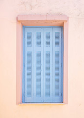 Greece, Kea island. Traditional wooden window shutters blue pastel color on pink painted wall in capital city of Ioulis.