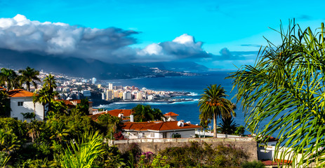 Naklejka premium Tenerife - Puerto de la Cruz is the tourist center of the island north coast on Tenerife. A view along the coast to the harbor town, on a sunny day with clouds gathering in October.