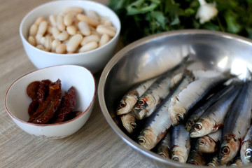 Fresh sardines, white beans, dried tomatoes and chicory on a wooden table. Ingredients for a meal. Selective focus.