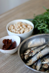Fresh sardines, white beans, dried tomatoes and chicory on a wooden table. Ingredients for a meal. Selective focus.