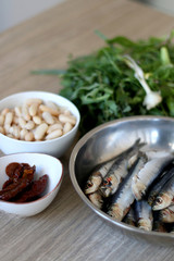 Fresh sardines, white beans, dried tomatoes and chicory on a wooden table. Ingredients for a meal. Selective focus.