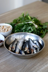 Fresh sardines, white beans, dried tomatoes and chicory on a wooden table. Ingredients for a meal. Selective focus.