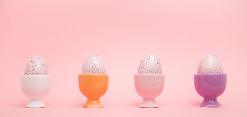 Row of speckled eggs in egg cups on pink