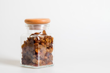 Close up. A glass jar with a wooden lid, contains raisins. White background. Copy space.