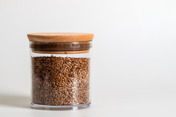Close up. A jar with a wooden lid, contains flax seeds. White background. Copy space.