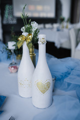 Served for wedding banquet table in blue white. Wedding decoration. Blue napkin with flower on a white plate. Golden bottles are vases for flowers. Decorated bottles of champagne.