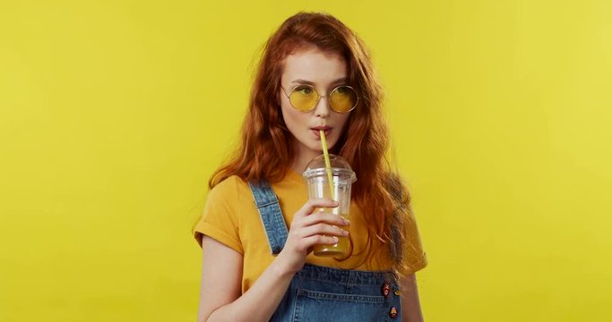 Close up of the beautiful Caucasian pretty girl with red hair in sunglasses smiling to the camera and drinking her drink, thn doing a face like she is boring.