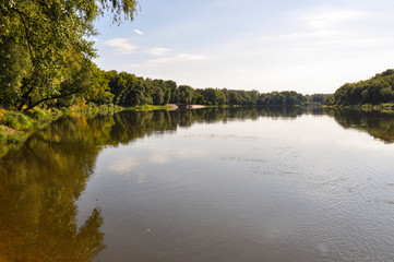 Wide yellow river is slow flowing. Early autumn. Sunny weather and brightgreen trees on the banks fron the both sides