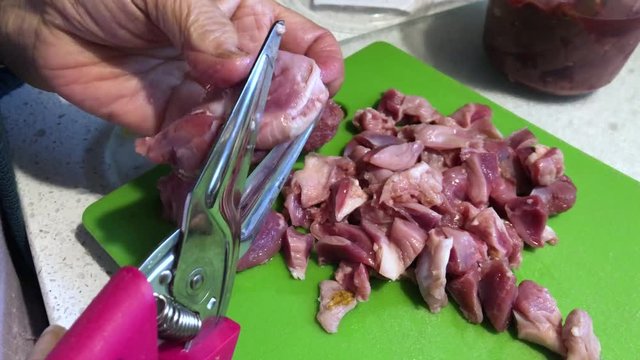 Closeup view of a cook chopping up liver gizzards with a pair of kitchen scissors.  	