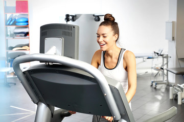 Treadmill training. A young woman in an exercise room is running on an automatic treadmill.
