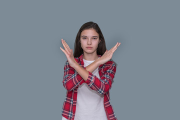 young teen girl with arms crossed, gesture stop, gray wall background