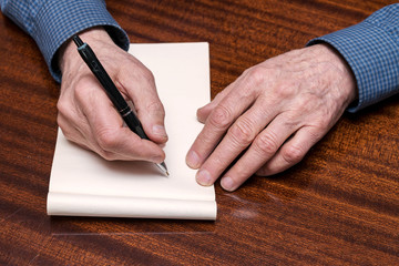 old man's hands with a pen, empty notebook for records, top view
