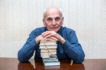 wise older man sitting at a table, hands folded on a pile of books
