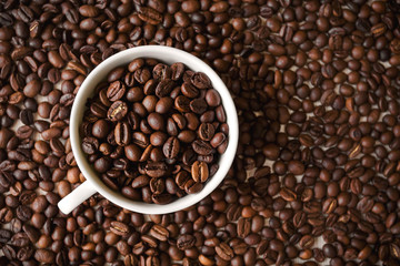 white cup with roasted coffee beans stands on the background of a large number of coffee beans