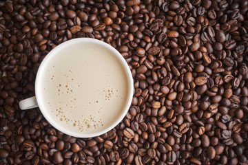 white cup with fragrant cappuccino with froth stands in coffee beans with free space on the right