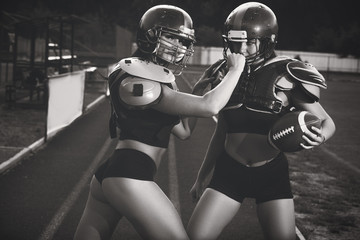 Sexy young sportive girls in uniform of rugby football player in action on the stadium. American football woman players on substitute,  tuned aggressively to fight, preparing to go on pitch