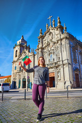 Young woman tourist with portuguese flag standing near the Congregados Carmelites church with famous portuguese blue tiles on the facade traveling in Porto city. Portugal