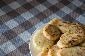 Hot tasty baked cheese pancakes in the plate standing on the  checkered tablecloth. Breakfast
