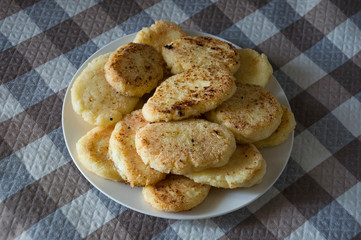 Hot tasty baked cheese pancakes in the plate standing on the  checkered tablecloth. Breakfast