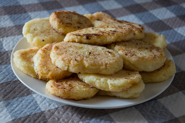Hot tasty baked cheese pancakes in the plate standing on the  checkered tablecloth. Breakfast