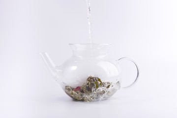 Pouring hot water to the glass teapot with herbal tea, isolated on white background