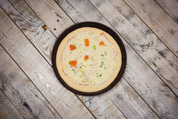 Round pizza dough is in the pan. The process of cooking pizza, stacking ingredients on the dough.