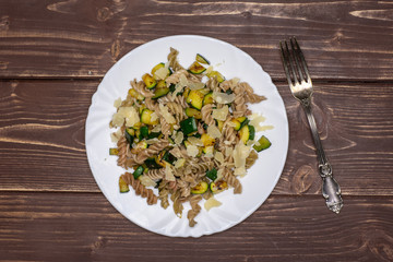 Ready to eat. recipe step by step fusilli pasta with zucchini on white porcelain plate with a fork flatlay on brown wood