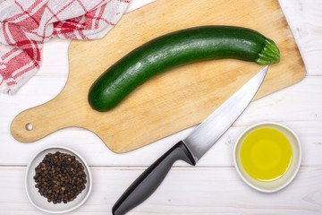 One whole zucchini is ready to be chopped. recipe step by step fusilli pasta with zucchini on chopping board with a knife and a tea towel flatlay on white wood