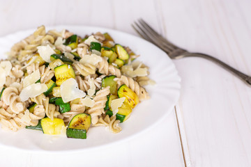 Recipe step by step fusilli pasta with zucchini closeup on white porcelain plate with a fork on white wood