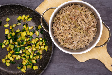 Mix boiled pasta with zucchini. recipe step by step fusilli pasta with zucchini on a frying pan with a stock pot on chopping board flatlay on grey stone