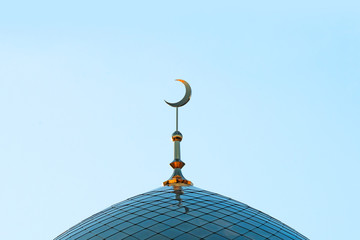 The Golden minaret of the mosque. Muslim symbol on blue sky background. Crescent. Sunset.