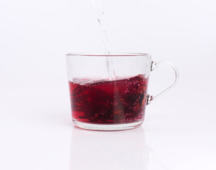 Pouring hot water to the glass cup with hibiscus tea, isolated on white background