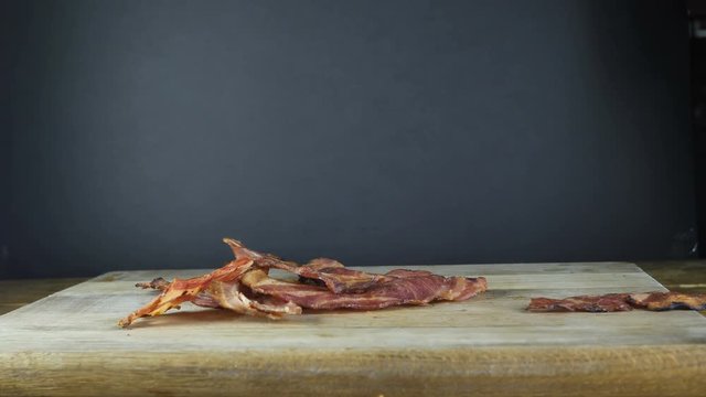 Closeup of fried bacon thrown on a wooden board that flies out beyond the borders of a wooden board, flying bacon, black isolated background
