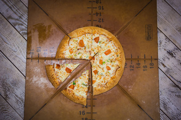 Appetizing large pizza cut into pieces, lying on the Board with numbers indicating its diameter 16cm. A piece of fresh pizza on a brown Board, hand takes pizza, cuts with a knife.