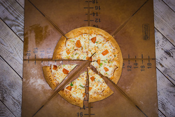 Fototapeta premium Appetizing large pizza cut into pieces, lying on the Board with numbers indicating its diameter 16cm. A piece of fresh pizza on a brown Board, hand takes pizza, cuts with a knife.