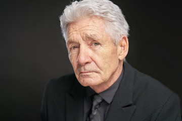 Old Man with grey har and black suit on black studio background