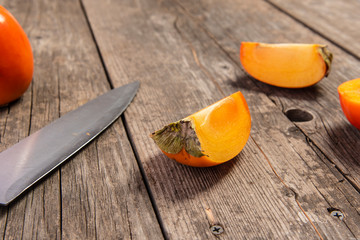 Particle of persimmon with knife on retro wooden table