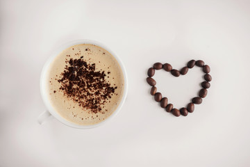 white cup with cappuccino and frothy and grated chocolate on a beige background and a heart with free space inside the coffee beans to the right of the cup
