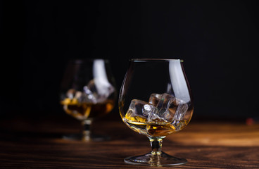 Two whiskey / cognac glasses with ice on a wooden background. Dark backdrop.