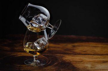 Two whiskey / cognac glasses with ice on a wooden background. Dark backdrop.