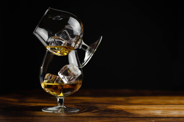 Two whiskey / cognac glasses with ice on a wooden background. Dark backdrop.
