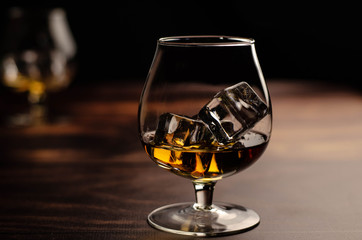 Two whiskey / cognac glasses with ice on a wooden background. Dark backdrop.