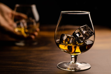 Whiskey / cognac glass with ice in a hand on a wooden background. Dark backdrop.