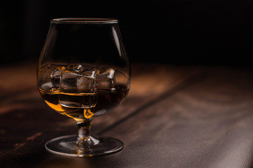 Whiskey / cognac glass with ice on a wooden background. Dark backdrop.