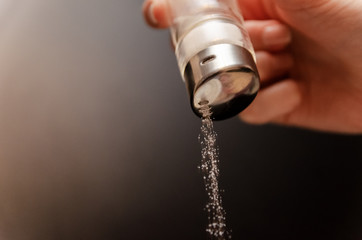 Sprinkle salt from a jar on a black background. Hand with a can of salt on a black background