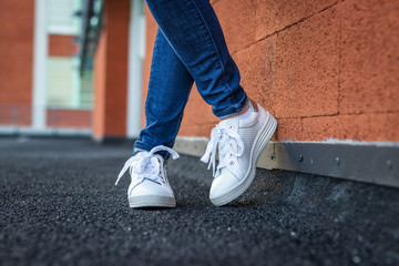 Female legs with jeans and white sneakers in city