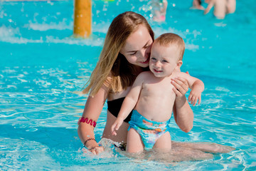 Fototapeta na wymiar Mother and baby in swimming pool. Parent and child swim in a tropical resort. Summer outdoor activity for family with kids. Vacation and traveling with young children. Inflatable toys for water fun
